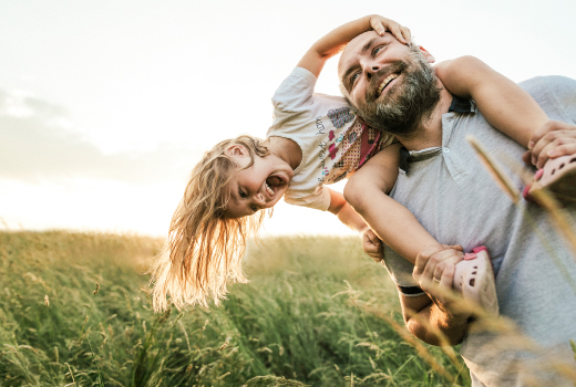 PIA Eine Person trägt ein Kind auf den Schultern in einer grünen Wiese bei Sonnenuntergang.
