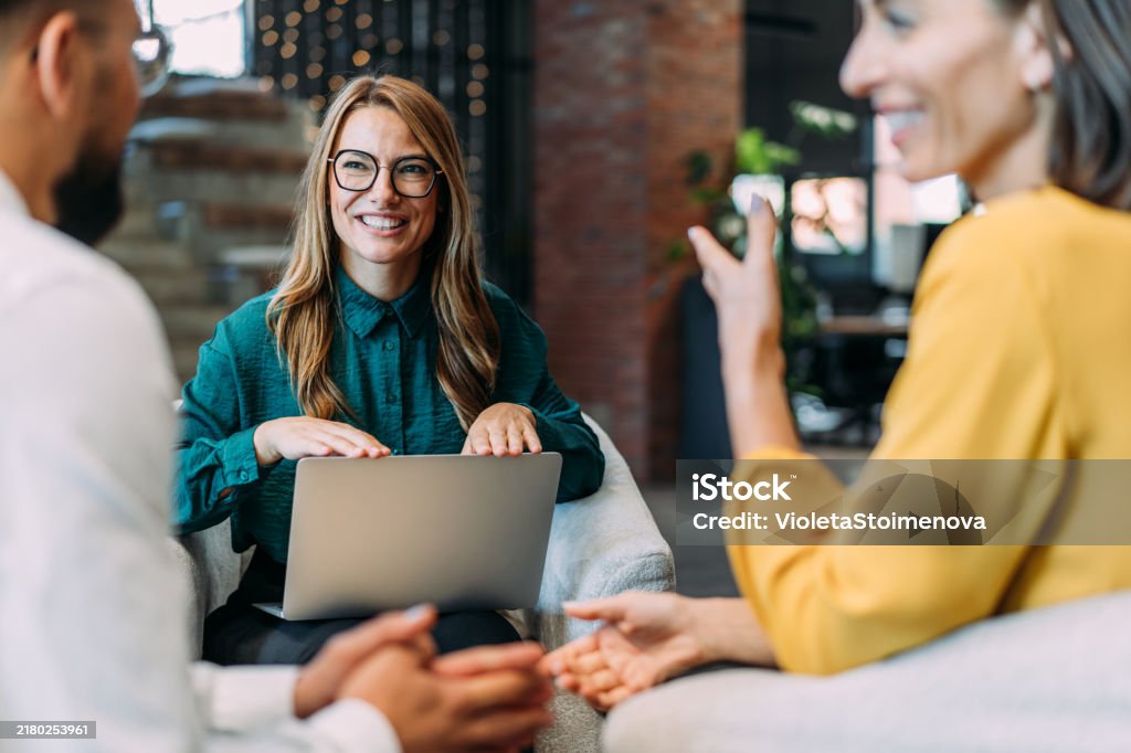 Drei Personen sitzen in einem modernen Raum und führen ein Gespräch. Eine Person hält einen Laptop und scheint zu präsentieren.